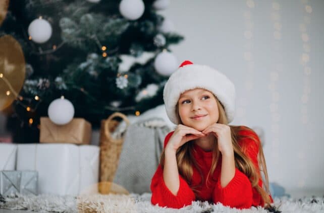 bambina con abiti natalizi vicino all'albero