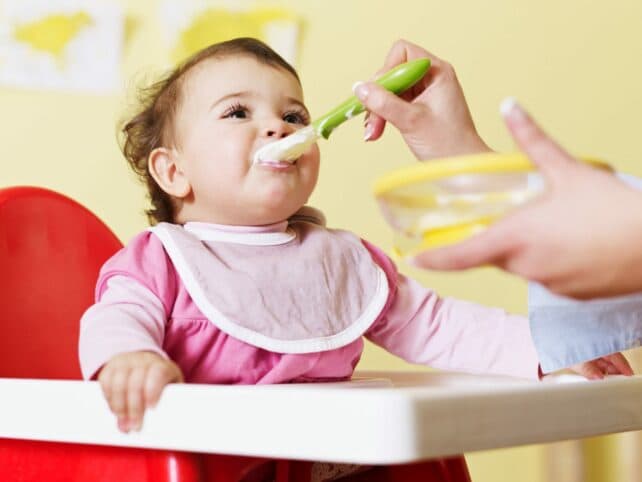 bambina che mangia la pappa nel seggiolone