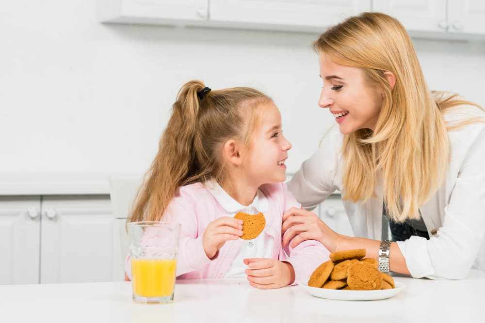 mamma e figlia in cucina con biscotti e succo di arancia